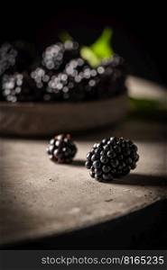 Ripe blackberries with leaves in a bowl on a dark rustic background. Ripe blackberries with leaves