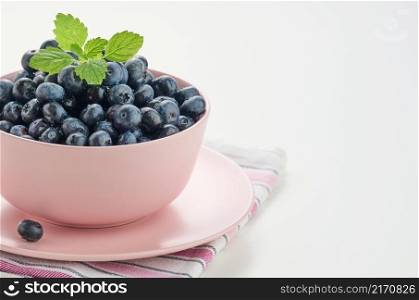Ripe blueberry in a pink ceramic plate on a white table, tasty and useful berry, copy space