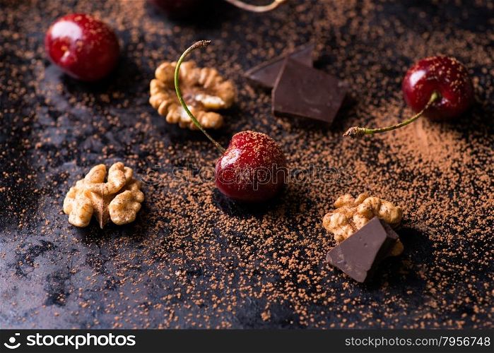 Ripe cherry, cocoa powder, walnuts, and chocolate chunks on dark background, selective focus