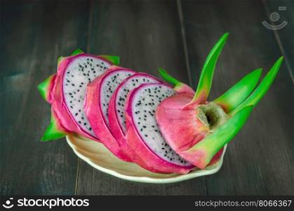 Ripe Dragon fruit with slice on dish over wooden background , still life