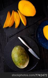 Ripe egyption Mango slices and whole mango served  at black dish. close up
