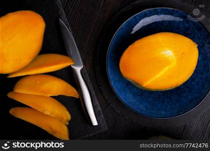Ripe egyption Mango slices served  at black dish and blue plate. close up