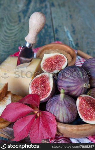 Ripe figs in a wooden bowl, cheese, cane sugar, honey and a checkered napkin on old cutting board as well as red autumn leaves lie on the old wooden table. Vertical photo