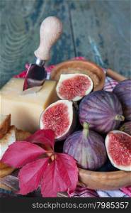 Ripe figs in a wooden bowl, cheese, cane sugar, honey and a checkered napkin on old cutting board as well as red autumn leaves lie on the old wooden table. Vertical photo