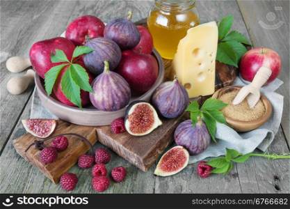 Ripe figs, red raspberry and apples, cane sugar, honey and a cheese on old cutting board as well as green leaves lie on the old wooden table