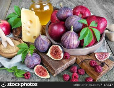Ripe figs, red raspberry and apples, cane sugar, honey and a cheese on old cutting board as well as green leaves lie on the old wooden table