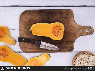 ripe fresh pumpkin on a brown wooden board and knife, next to a bowl with pumpkin seeds, top view