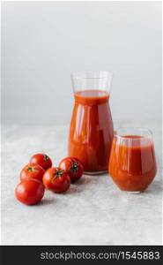 Ripe fresh red tomatoes near two glasses of squezeed tasty tomato juice, against white background. Ingredients. Healthy vegetables
