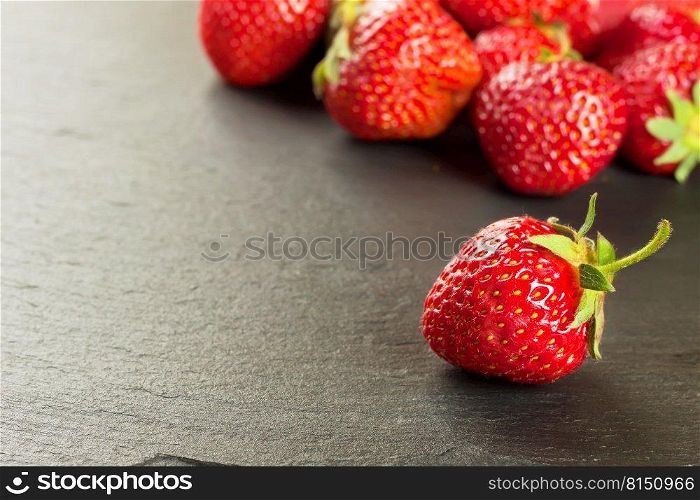 Ripe fresh strawberries scattered on a black slate surface. Mockup with copy space for text.. Ripe fresh strawberries on black slate background