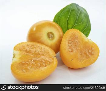 ripe golden berries, one cut in half and one whole accompanied by a mint leaf, on a white background Macro shot.