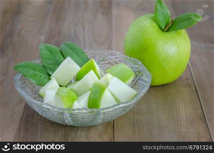 Ripe green apple with leaf and slice on a wooden background