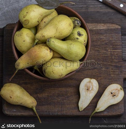 ripe green pears in a brown clay bowl on a table, top view