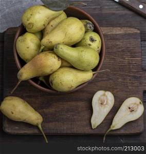 ripe green pears in a brown clay bowl on a table, top view