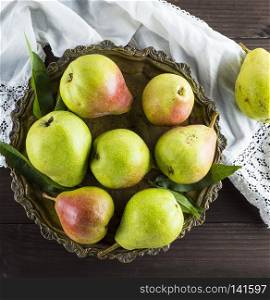 ripe green pears in an iron plate on a brown wooden table, top view