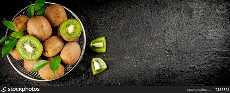 Ripe kiwi with leaves in a colander on the table. On a black background. High quality photo. Ripe kiwi with leaves in a colander on the table.