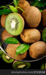 Ripe kiwi with leaves in a colander on the table. On a black background. High quality photo. Ripe kiwi with leaves in a colander on the table.