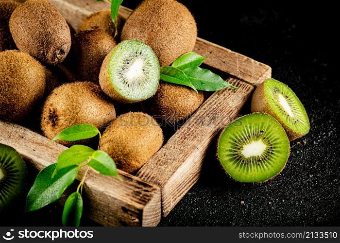 Ripe kiwi with leaves on a wooden tray. On a black background. High quality photo. Ripe kiwi with leaves on a wooden tray.