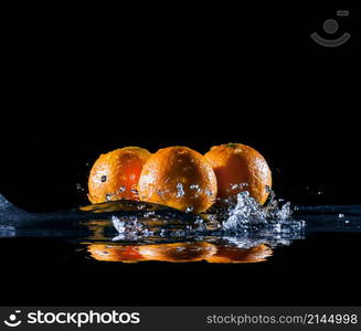 ripe oranges lying on mirror in sprays and splashes of water on dark background. ripe oranges in water