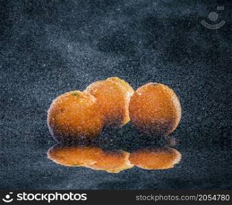 ripe oranges lying on mirror in sprays of water on dark background. ripe oranges in water