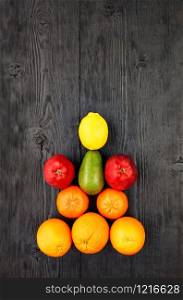 Ripe oranges, tangerines, apples, avocados and lemon lie symmetrically on an old black wooden surface, flat lay, image with copy space, in vertical image.. Ripe fruits and citrus fruits lie symmetrically on an old black wooden table.
