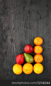 Ripe oranges, tangerines, apples, avocados lie on an old black wooden surface, flat lay, image with copy space.. Ripe fruits and citrus fruits lie on an old black wooden table.