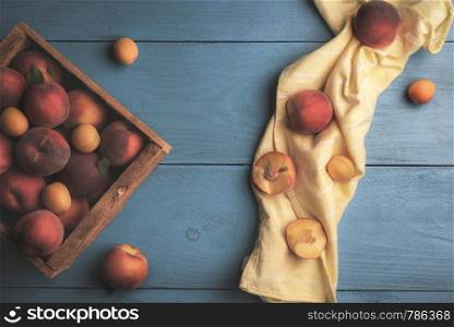 Ripe peaches and apricots harvested in a wooden box, above view on a blue table and a yellow kitchen towel. Flat lay of fresh fruits in a vintage box.
