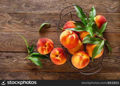 Ripe peaches with leaves in basket on wooden table, top view