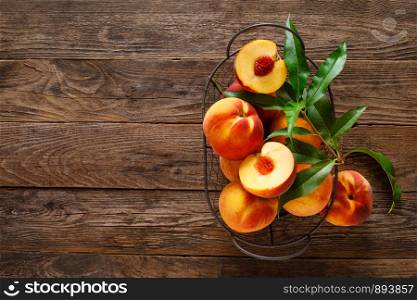 Ripe peaches with leaves in basket on wooden table, top view