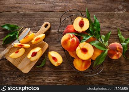 Ripe peaches with leaves in basket on wooden table, top view