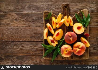 Ripe peaches with leaves on wooden board, top view