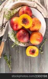 Ripe peaches with thyme leaves in a plate on a wooden board on a background