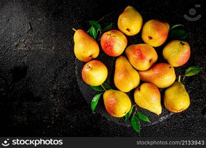 Ripe pears with leaves on a stone board. On a black background. High quality photo. Ripe pears with leaves on a stone board.