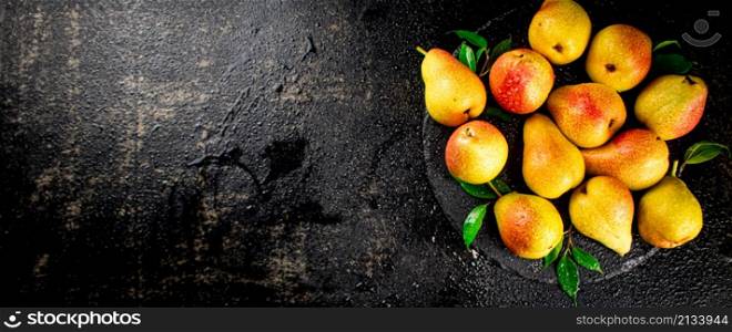 Ripe pears with leaves on a stone board. On a black background. High quality photo. Ripe pears with leaves on a stone board.