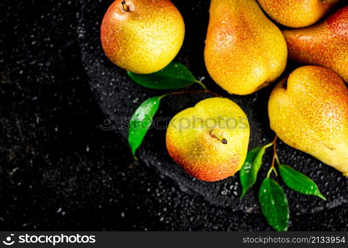 Ripe pears with leaves on a stone board. On a black background. High quality photo. Ripe pears with leaves on a stone board.