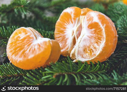Ripe peeled slices of tangerine without peel lie on the green branches of a Christmas tree. Citrus fruits, tangerines or oranges. Close-up.. Ripe peeled slices of tangerine without peel lie on the green branches of a Christmas tree.