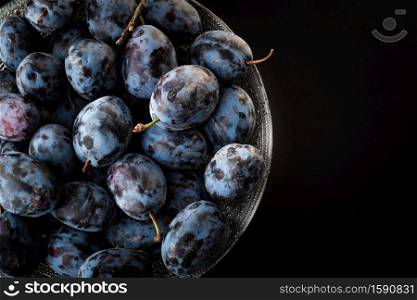 Ripe Plums in bowl. Top view against black background. Copy space on right. Ripe Plums in bowl. Top view against black background