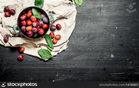 Ripe plums in bowl with leaves. On a black chalkboard.. Ripe plums in bowl with leaves.