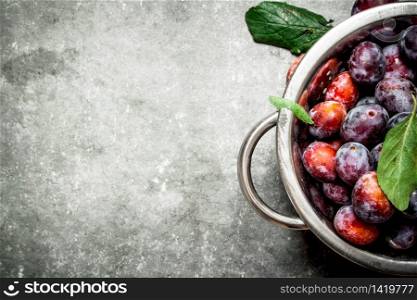 Ripe plums with green leaves. On a stone background.. Ripe plums with green leaves.