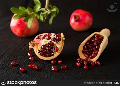 Ripe pomegranate fruits and bailer with seeds inside over a black textured background. Ripe pomegranate fruits and bailer with seeds inside
