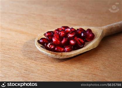 Ripe pomegranate seeds in wooden spoon