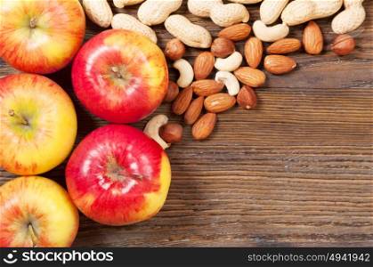 Ripe red apples and different nuts on a wooden background. Top view.