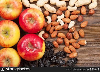 Ripe red apples, dried plums and different nuts on a wooden background. Top view.
