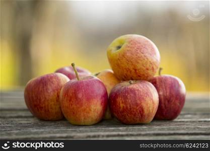 Ripe red apples on a wooden table, on green outdoor background