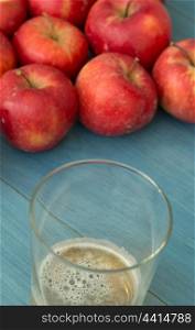 Ripe red apples with a glass of cider blue table close up