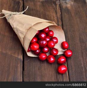 Ripe red cherry in a paper bag on a brown wooden background