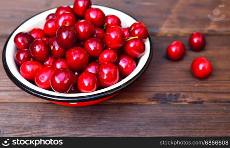 Ripe red cherry in an iron bowl on a brown wooden table