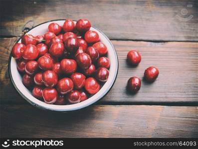 Ripe red cherry in an iron plate on a brown table, vintage toning