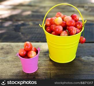 Ripe red cherry in iron buckets on a brown wooden table, top view