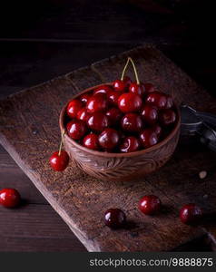 ripe red juicy sweet cherry in a brown clay bowl on a wooden table, close up