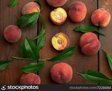 ripe red peaches and green leaves on a brown wooden table, top view